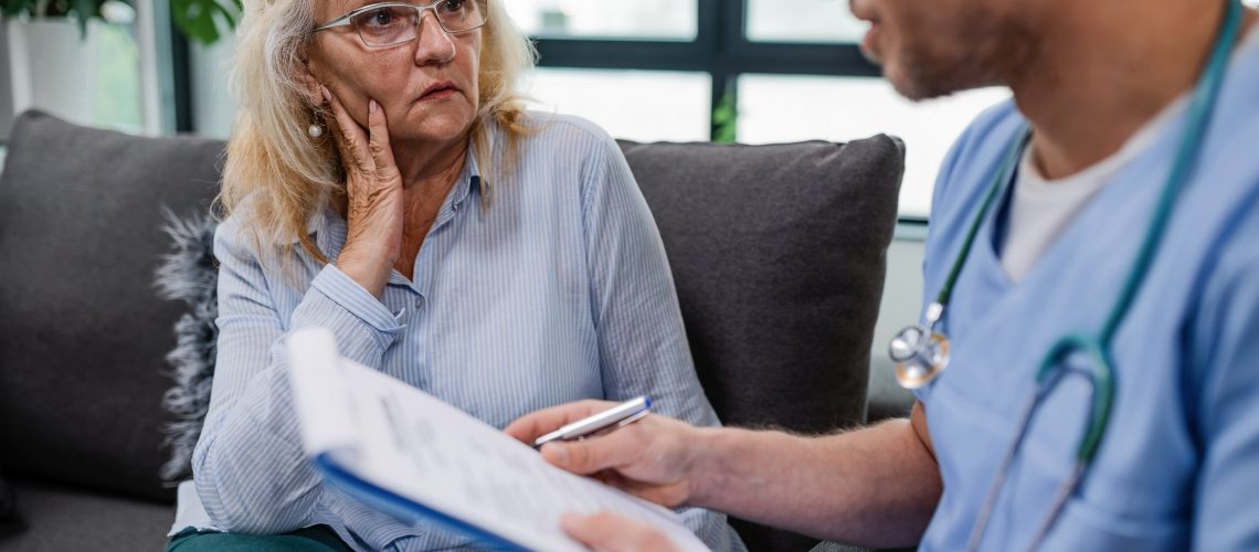 Senior woman communicating with healthcare worker about her medical reports during a home visit.